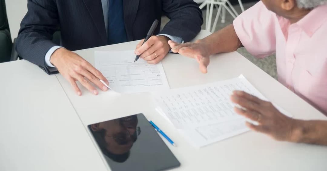 Business professional and senior reviewing medicare guide program documents at table with tablet.