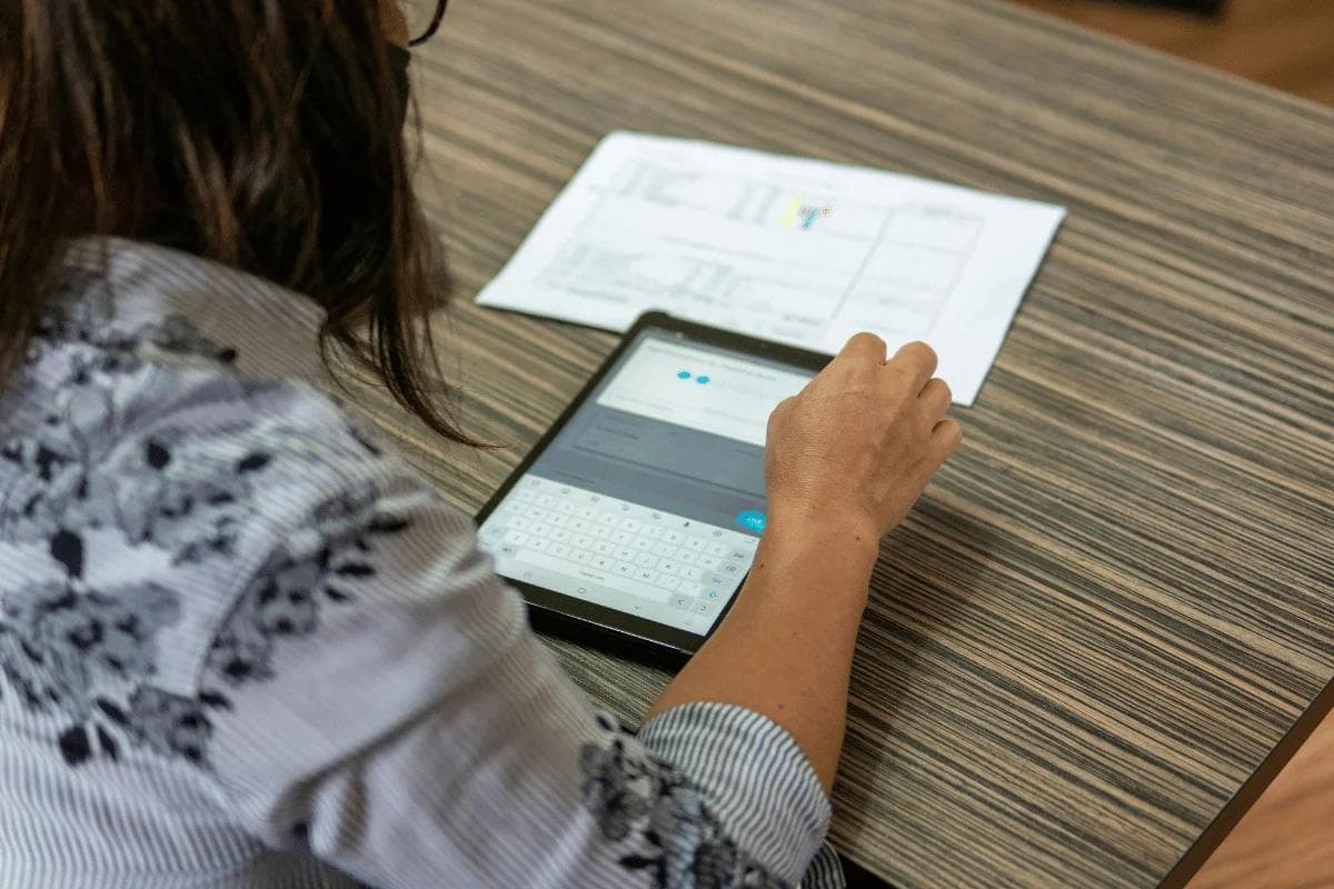 Business professional using a tablet while reviewing printed financial documents.