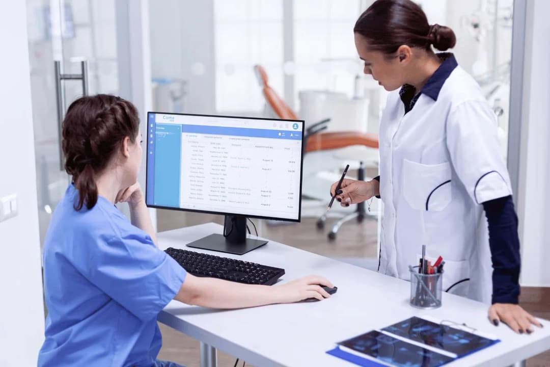 Two medical professionals review patient information on a computer in a clinical office setting.