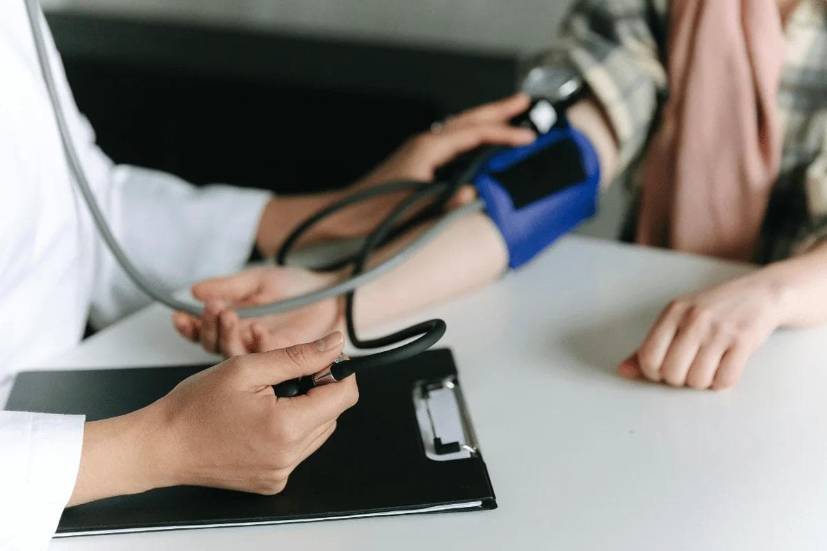 Doctor checking patient’s blood pressure with cuff and stethoscope.