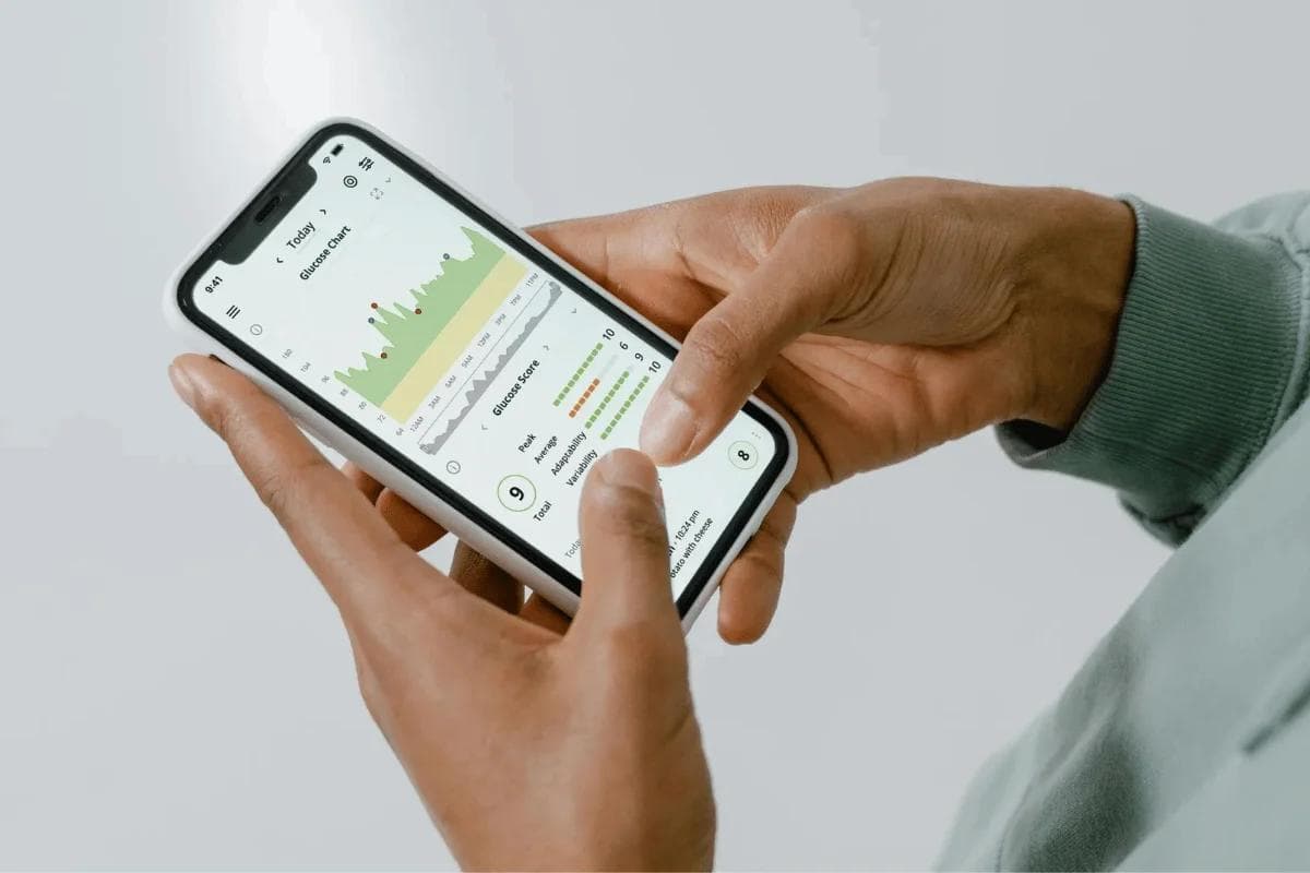 Close-up of hands holding a smartphone displaying a fitness app with a green activity chart and scores. The tone is focused and informative.