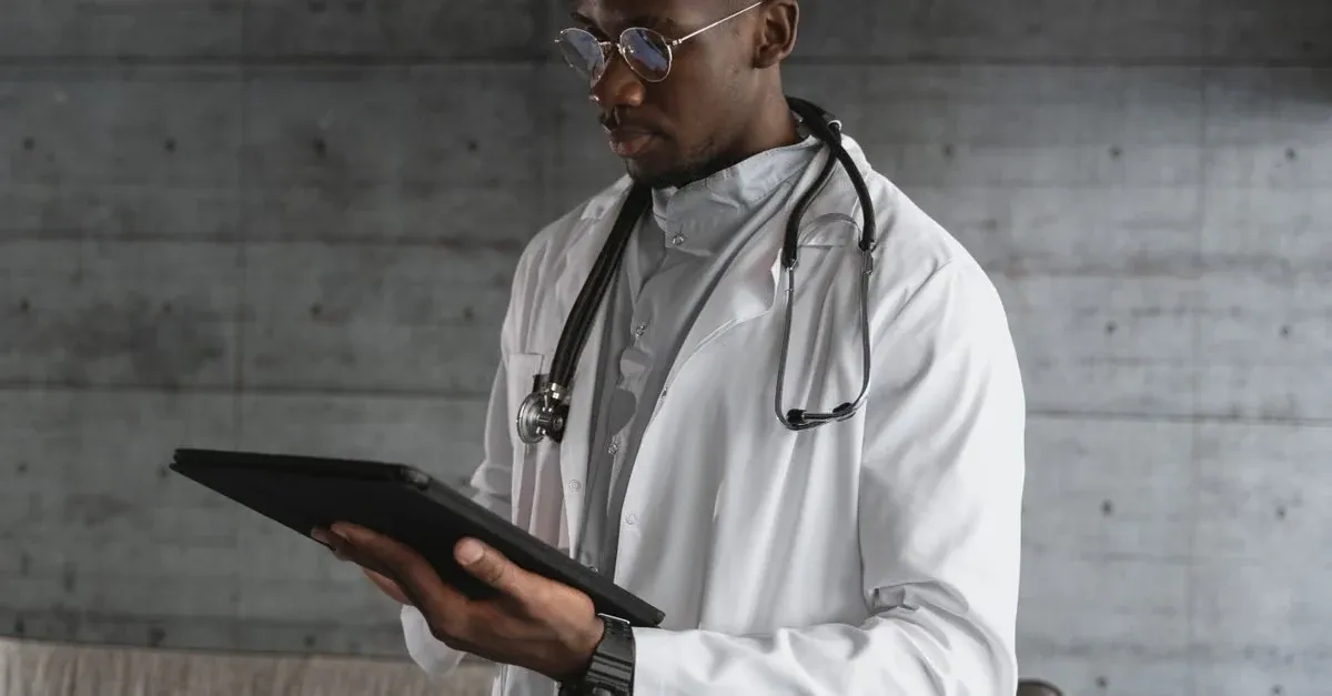 Doctor in white coat reviewing patient data on tablet for remote patient monitoring primary care consultation.