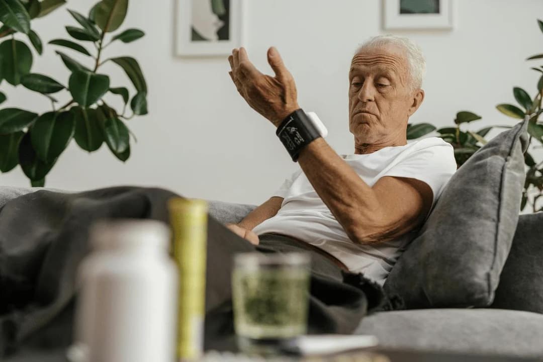 Older man sitting on couch checking his blood pressure monitor at home.