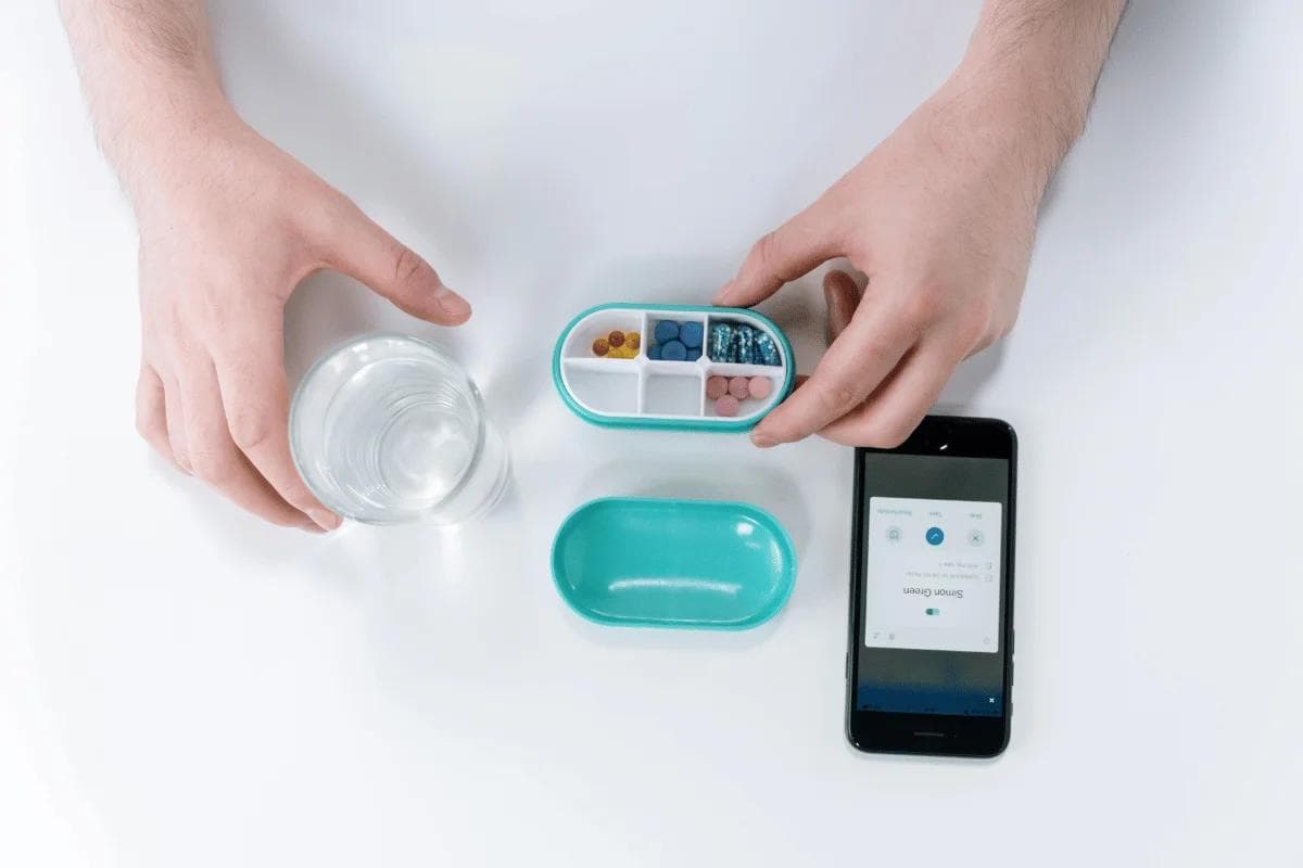 Person organizing pills in a smart pillbox with phone app.