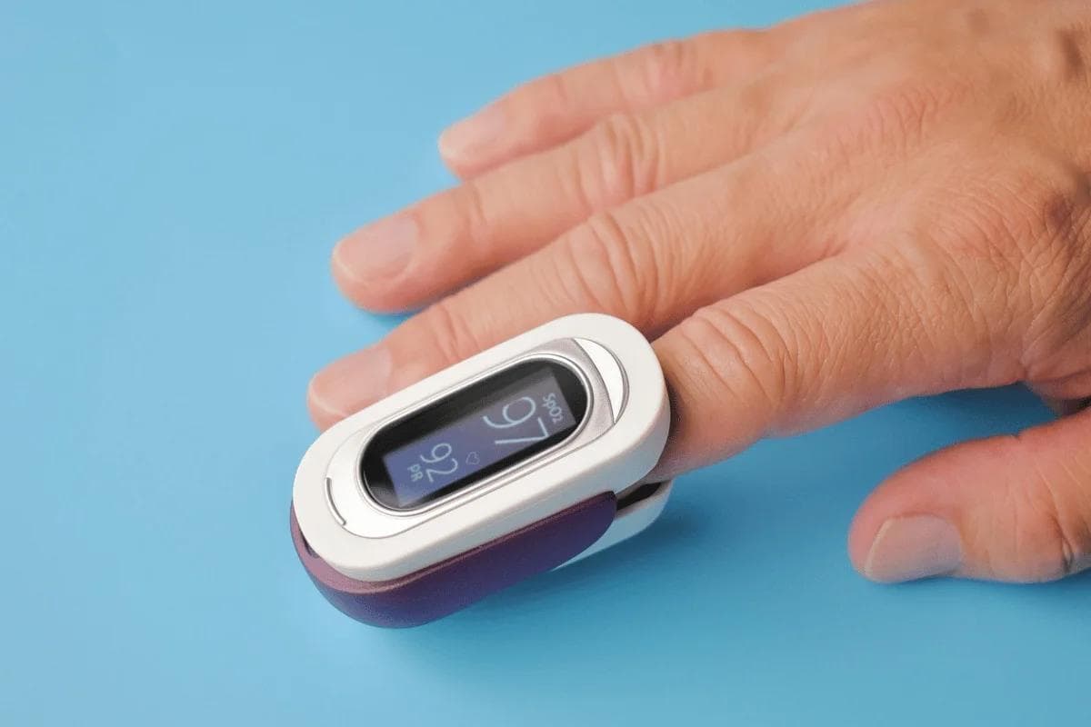 Close-up of a hand with a white and purple pulse oximeter on a finger, displaying 97% SpO2. The background is a bright blue, conveying a calm, medical setting.