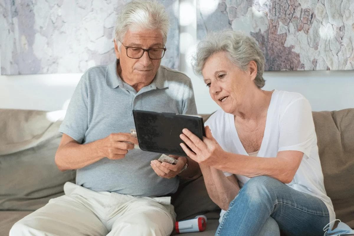 Elderly couple sitting on a couch, engaged with a tablet.