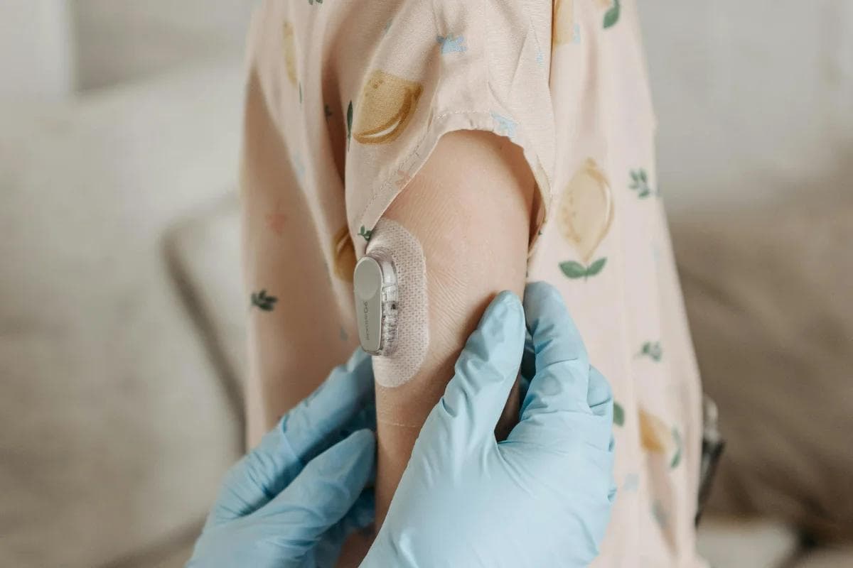 A person with a continuous glucose monitor on their arm, wearing a fruit-patterned shirt.