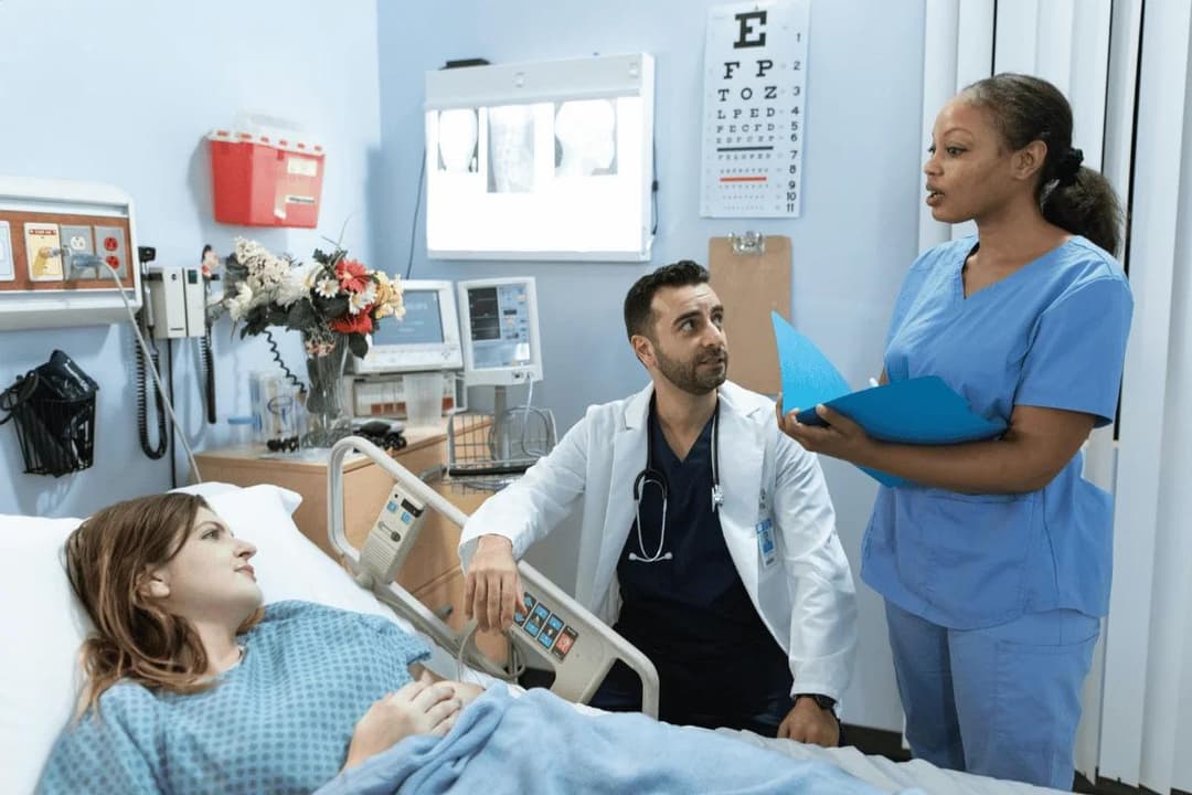 Doctor and nurse discuss a patient’s chart bedside, reflecting compassionate hospital care and teamwork.