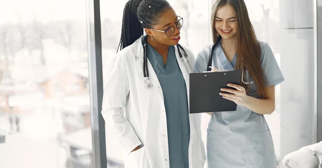 Two healthcare professionals smile while reviewing a clipboard.