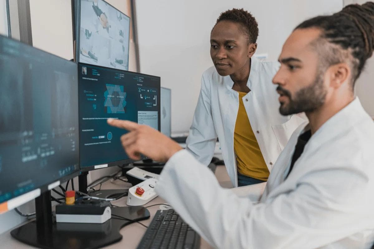 Two scientists in lab coats analyze data on computer screens, collaborating in a focused modern research lab.