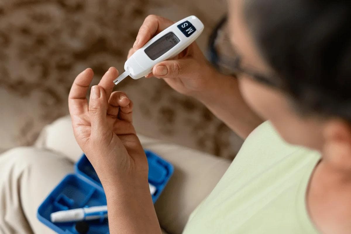 A person using a blood glucose meter, preparing to check their blood sugar levels, with a blue testing kit visible nearby.